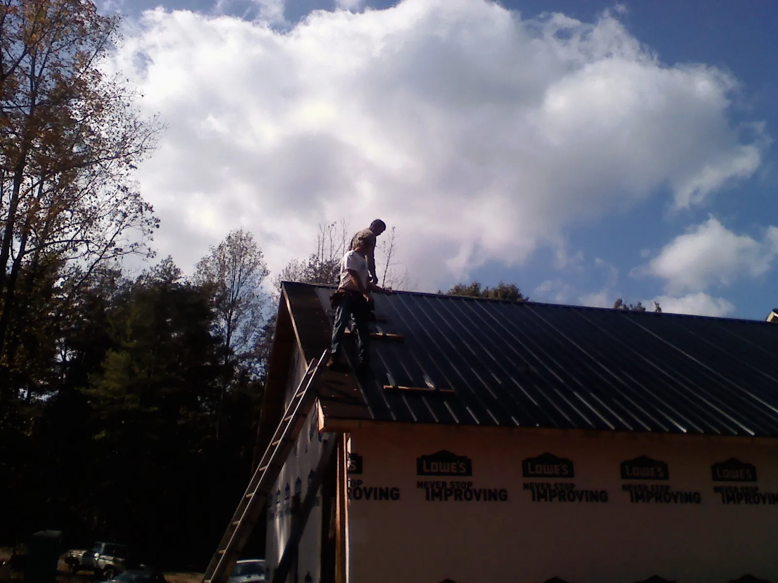 Roofer fastening dark metal panels high against a cloudy sky, from a Roof Inspection job in Hoodsport