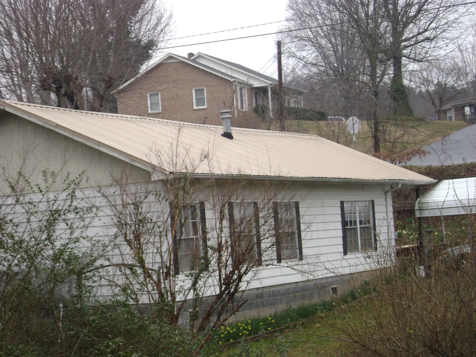 Tan metal roof on a white sided house set into a hillside — Commercial Roofing by Roofing Brothers in Hoodsport